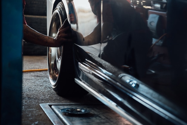 Car mechanic or serviceman disassembly and checking a car alloy chrome wheel