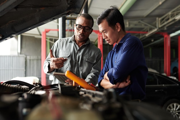 Car mechanic talking to owner showing him results of diagnostics