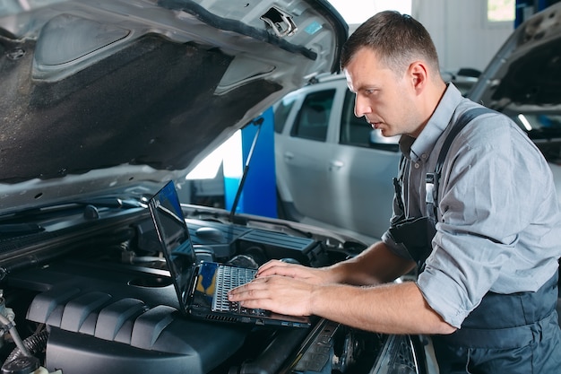 Meccanico di automobile che utilizza un computer portatile per diagnosticare e controllare il motore dell'auto