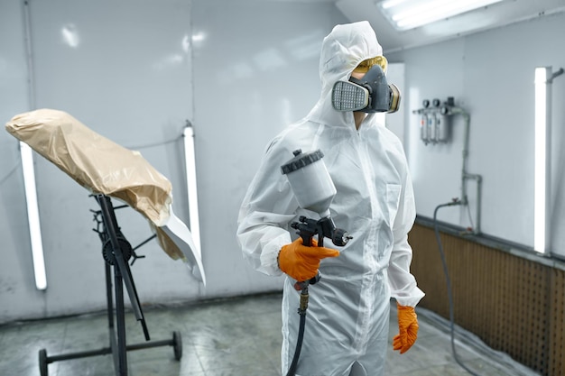 Car mechanic wearing safety clothes and respiratory mask leaving paint chamber after finished work