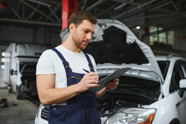 Car mechanic writing while holding clipboard near cars