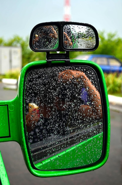 Car mirror in raindrops. Close up. Green side mirror on the car. Journey. Summer rainy weather. Selective focus.