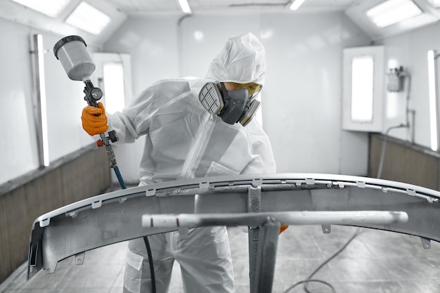 Car painter wearing protective clothes, mask painting\
automobile door using sprayer