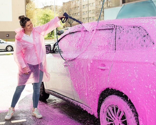 Photo car in pink foam at the car wash, a woman happily washes her car