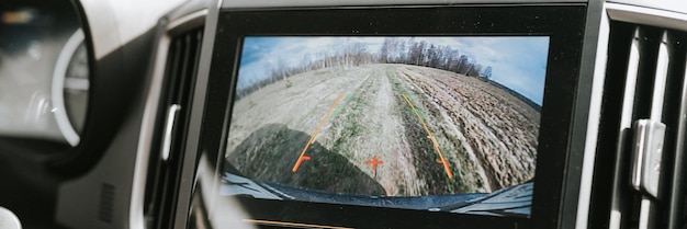Автомобильная система заднего вида, монитор, экран видеокамеры заднего вида, современное цифровое технологическое оборудование на автомобильной приборной панели для обеспечения безопасности дорожного движения по дикой сельской грязной грунтовой дороге в поле, лесной баннер