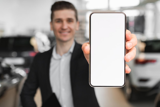 Менеджер приложения по аренде автомобилей в дилерском центре показывает смартфон с пустым экраном