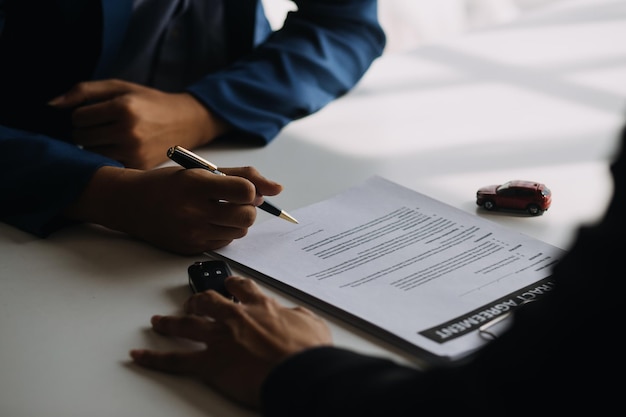 A car rental company employee is handing out the car keys to the renter after discussing the rental details and conditions together with the renter signing a car rental agreement Concept car rental