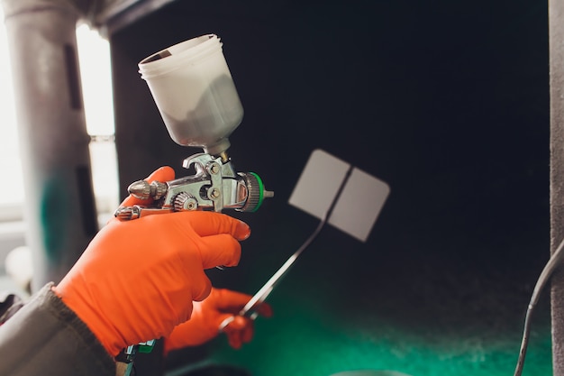 Car repair service. Worker painter checking color matching before painting. spraying black liquid onto the fitting plate.