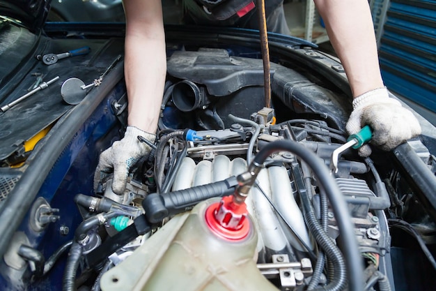 Foto un riparatore di auto svita parti con una chiave inglese con manico verde nel vano motore come candele e bobine di accensione in un'officina di riparazione di veicoli industria dei servizi automobilistici