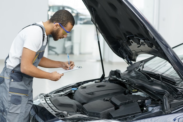 Scrittura del riparatore dell'automobile sulla sua lavagna per appunti mentre lavorando al garage