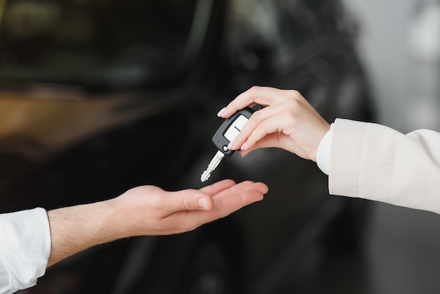 Car sale Dealer giving key to new owner in auto show or salon closeup