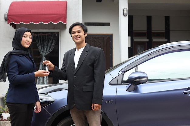 Car salesman handing over new car key to muslim woman customer.