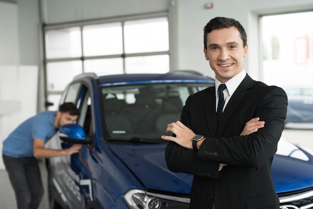 A car salesman is posing for a camera near buyers.