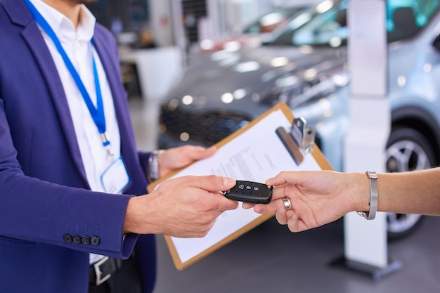 Car salesman sells a car to happy customer in car dealership and hands over the keys