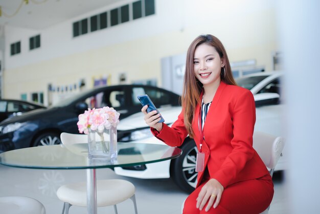 Car salesmen, beautiful women, Asian women who are talking on the phone with customers to sell new cars in car showrooms