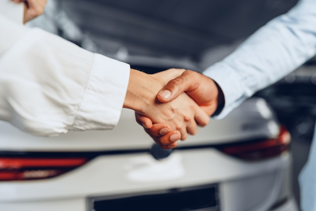 Car seller and buyer handshake against a car