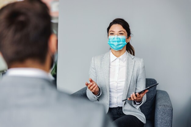 Car seller sitting with a customer in car salon and talking about promotions. Corona virus outbreak.