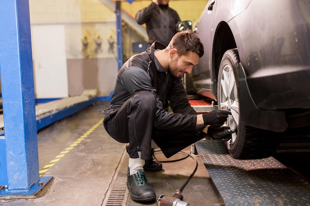 Foto riparazione auto manutenzione e persone concetto meccanico auto uomo con cacciavite elettrico cambio pneumatici in officina