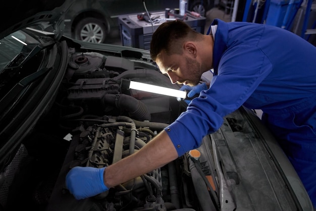 car service, repair, maintenance and people concept - auto mechanic man with lamp working at workshop