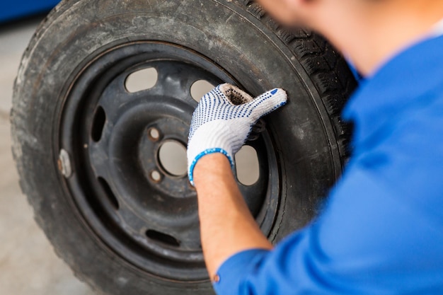 car service, repair, maintenance and people concept - auto mechanic man with wheel tire at workshop