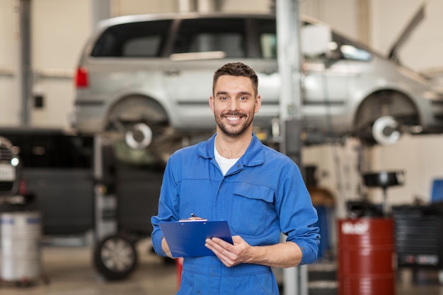 car service, repair, maintenance and people concept - happy smiling auto mechanic man or smith with clipboard at workshop