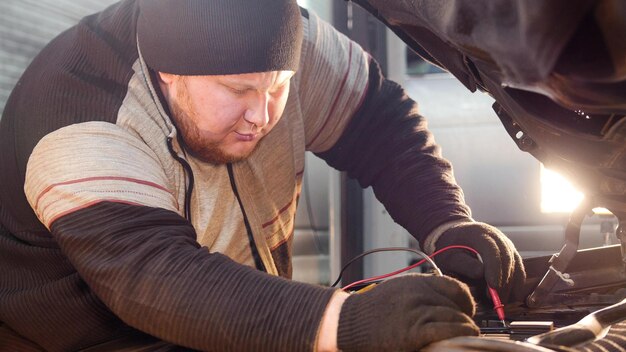 車のサービスの厚い生姜のメカニックの男は、マルチメーターで電圧をチェックします