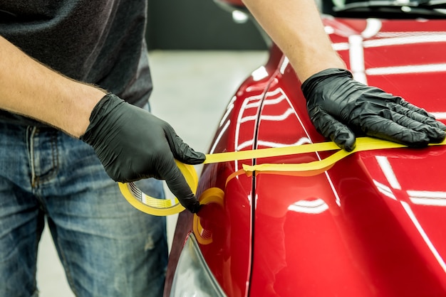 Car service worker applying protective tape on the car details before polishing.