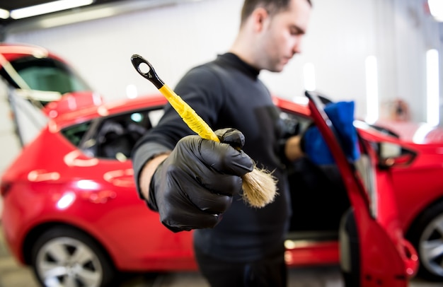 Car service worker cleans interiror with special brush