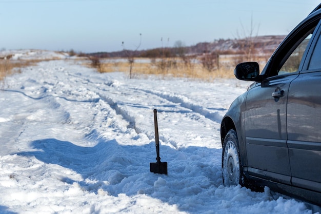 Car stuck in snow offroad at daylight with shovel and selective focus