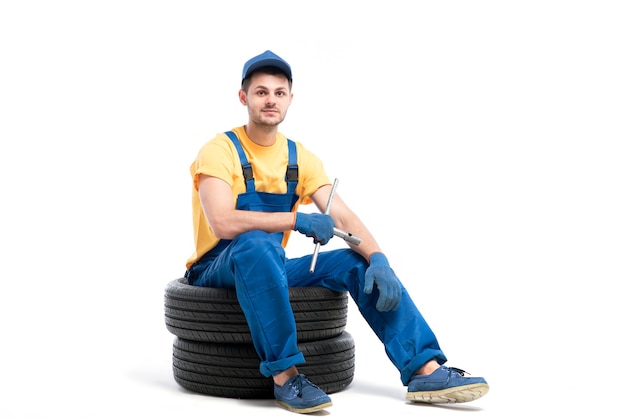 Car tire service, worker in blue uniform sitting on car tyres, white, repairman, wheel mounting