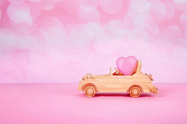 Car toy with a gift and a bow in the form of a heart on a pink background with bokeh