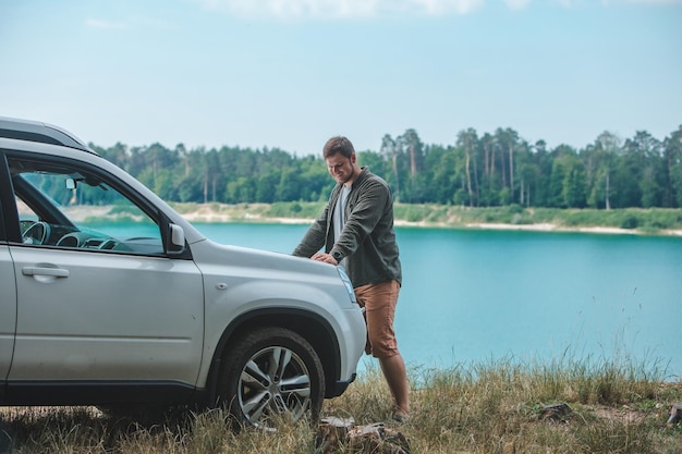 Car travel concept man looking on the man at suv car hood lake on background