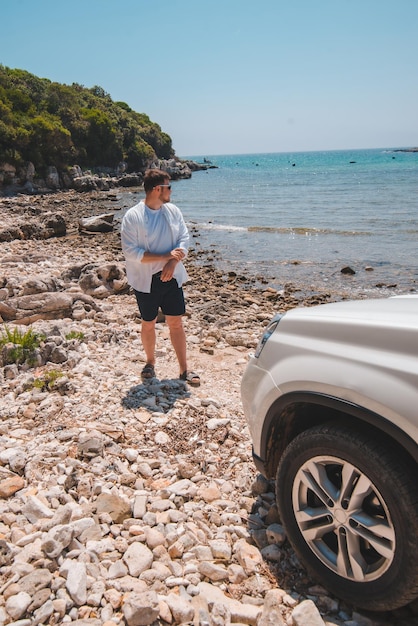 Uomo di concetto di viaggio in auto alla spiaggia estiva guardando il mare