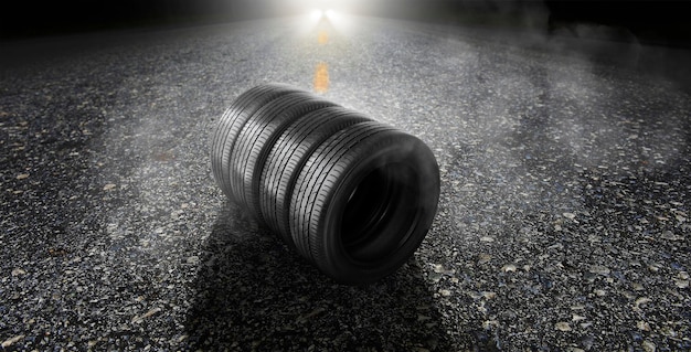 Car tyre on an asphalt road with smoke and a car headlight on the background at night