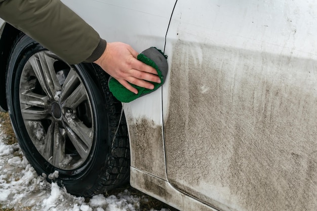 水石鹸スポンジで洗車家の裏庭の屋外の冬に汚れの自動車のぼろきれを掃除する男