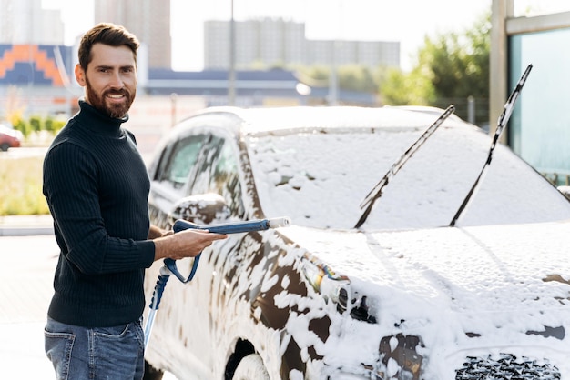 Car washing Waist up portrait view of the caucasian man holding special equipment and smiling to the camera Cleaning car using high pressure water concept Selective focus