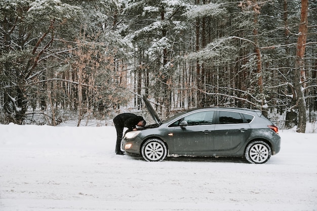 A car with an open hood on the background of a winter forest