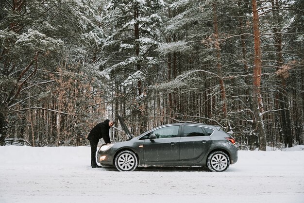 A car with an open hood on the background of a winter forest