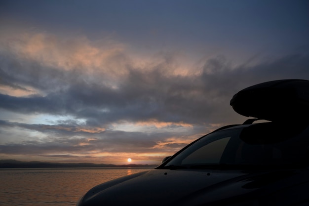 바다 위로 일출을 배경으로 화물 상자가 있는 트렁크가 있는 자동차.