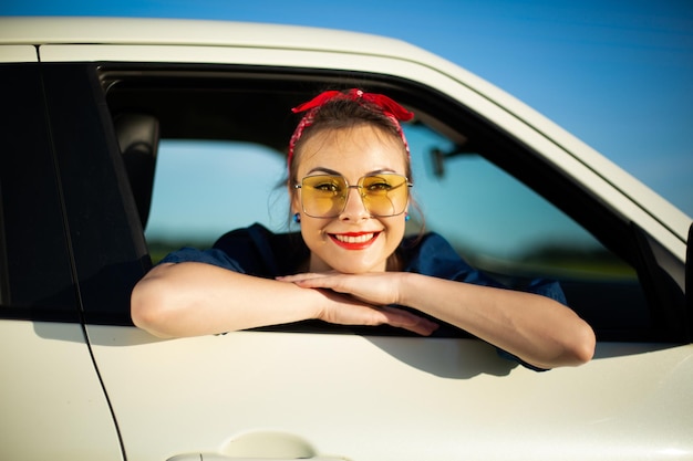 窓の外で幸せな笑顔を振ってロードトリップで道路上の車の女性