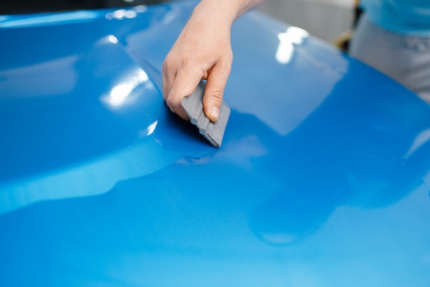 Photo car wrapping, mechanic with squeegee installs film