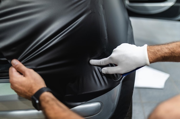 Car wrapping specialist putting vinyl foil or film on car. Selective focus.