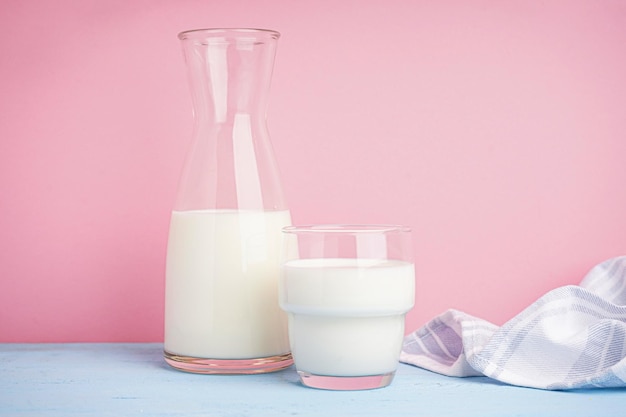 Photo carafe and glass of fresh milk on light pink background