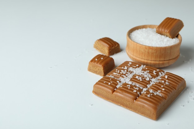 Caramel and bowl of salt on white background