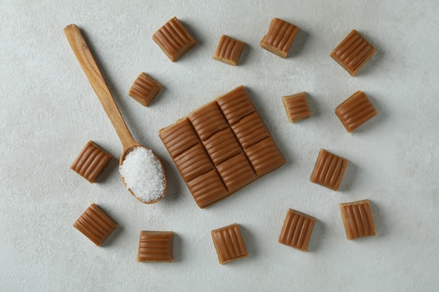 Caramel pieces and spoon with salt on white textured background