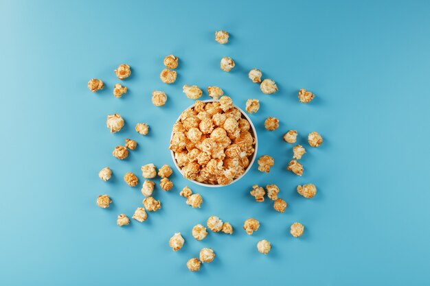 Caramel popcorn in a white glass cup with scissors on a blue surface. A delicious catch for filming movies, TV series, cartoons. Free legal, crimes.