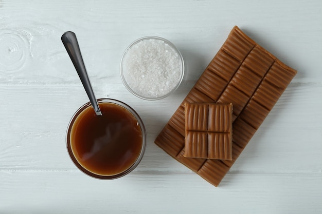 Caramel sauce, bar and salt on white wooden background