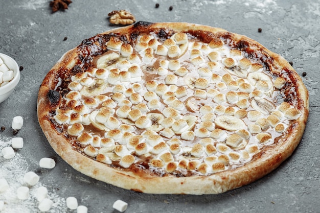 Banana caramellata con crema di nocciole pizza. gli ingredienti sono pasta per pizza, banana a fette e crema di nocciole. dolce e croccante.