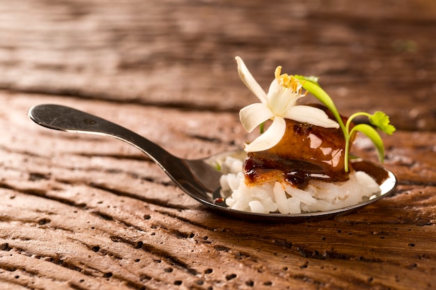 Foto maiale caramellato accompagnato da riso al gelsomino e curry rosso in un cucchiaio. assaggia il fingerfood della gastronomia