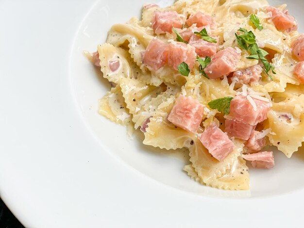 carbonara farfelle pasta with ham sausage on white plate